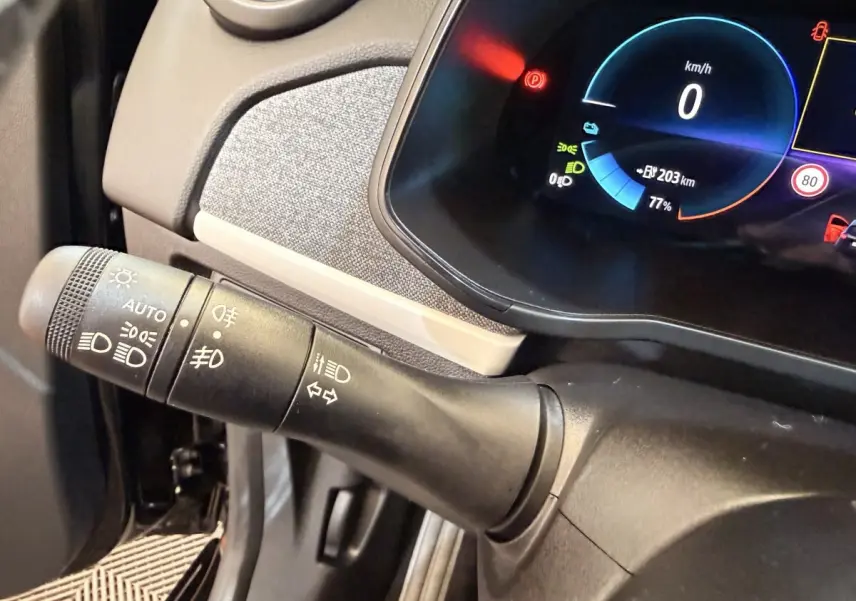 Gros plan sur la manette de commande des phares et clignotants à gauche du tableau de bord numérique bleu de la Renault ZOE noire.