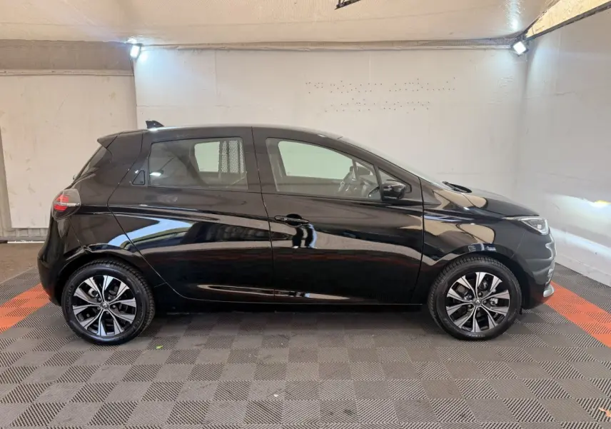 Profil droit d'une Renault ZOE noire 2024 avec jantes alliage distinctives dans un garage éclairé.