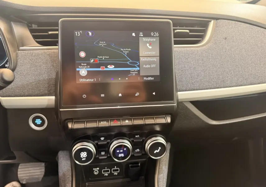 Vue intérieure centrée sur l’écran tactile et la console de la Renault ZOE noire, avec commandes climatisation et bouton démarrage.