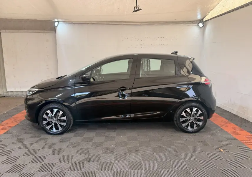 Renault ZOE noire vue de profil côté gauche, avec jantes alliage et lignes fluides, en intérieur éclairé.