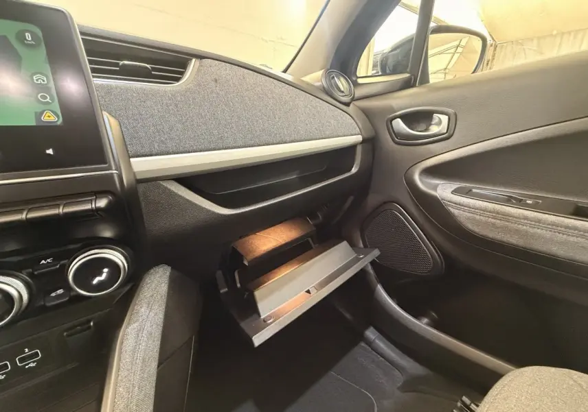 Intérieur Renault ZOE noir, vue côté passager avec boîte à gants ouverte et tableau de bord gris texturé.