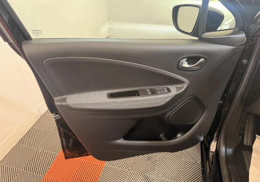 Vue intérieure de la porte avant gauche noire de la Renault ZOE 2024 avec accoudoir tissu gris et commandes électriques.