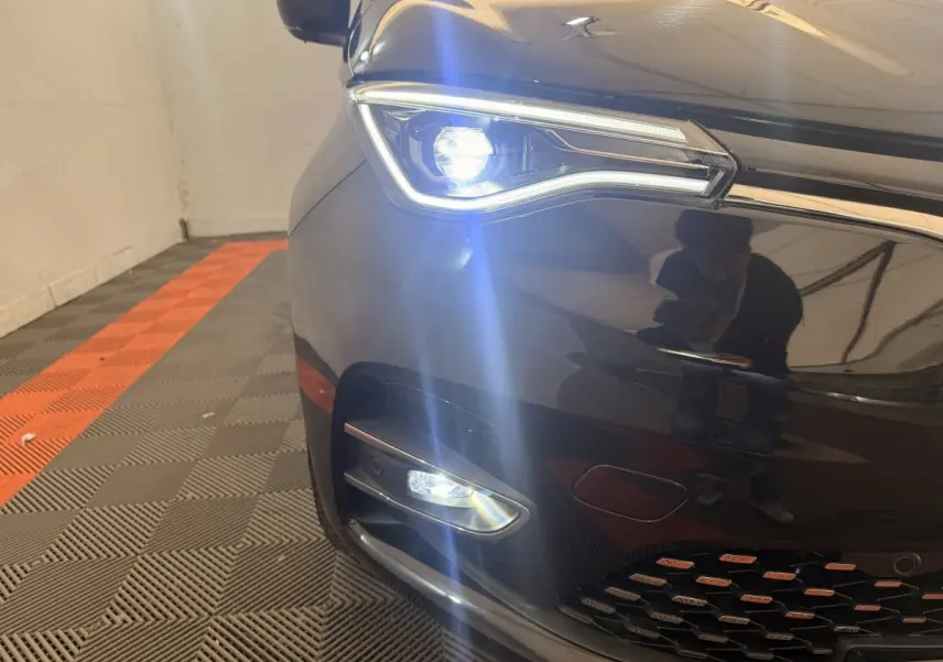 Gros plan sur l'avant droit noir de la Renault ZOE 2024 avec phares LED allumés et calandre visible.