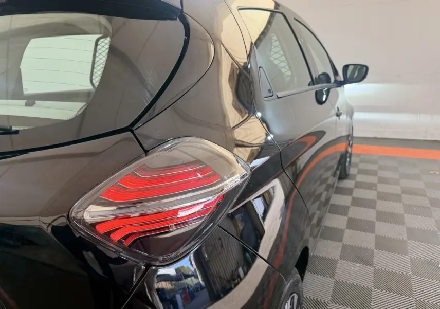 Vue 3/4 arrière droite d'une Renault ZOE noire 2024 avec feux arrière LED distinctifs dans un parking couvert.