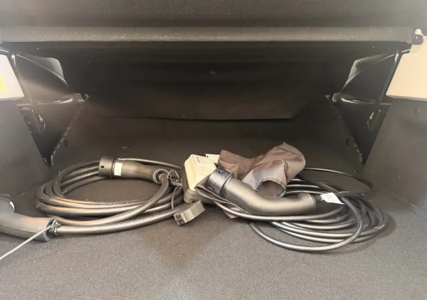 Coffre ouvert d'une Renault ZOE noire avec câble de charge électrique enroulé visible au centre.