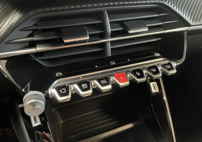 Vue rapprochée de la console centrale noire brillante du Peugeot 2008 bleu, avec commandes tactiles et boutons chromés.