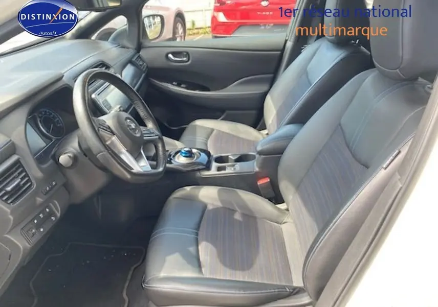 Intérieur du Nissan Leaf électrique blanc nacré, vue côté conducteur sur les sièges en cuir et tableau de bord moderne.