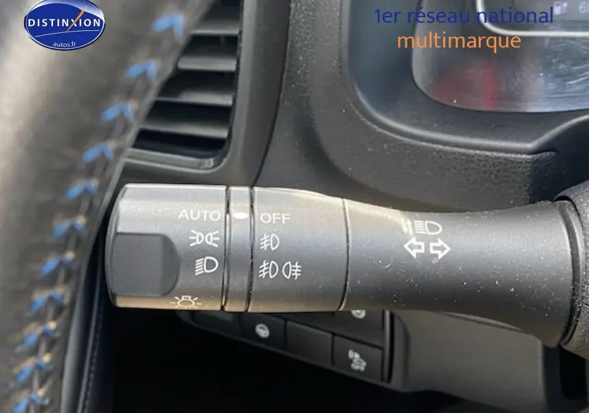 Gros plan sur la commande des feux et clignotants à gauche du volant d'une Nissan Leaf blanche nacrée électrique.
