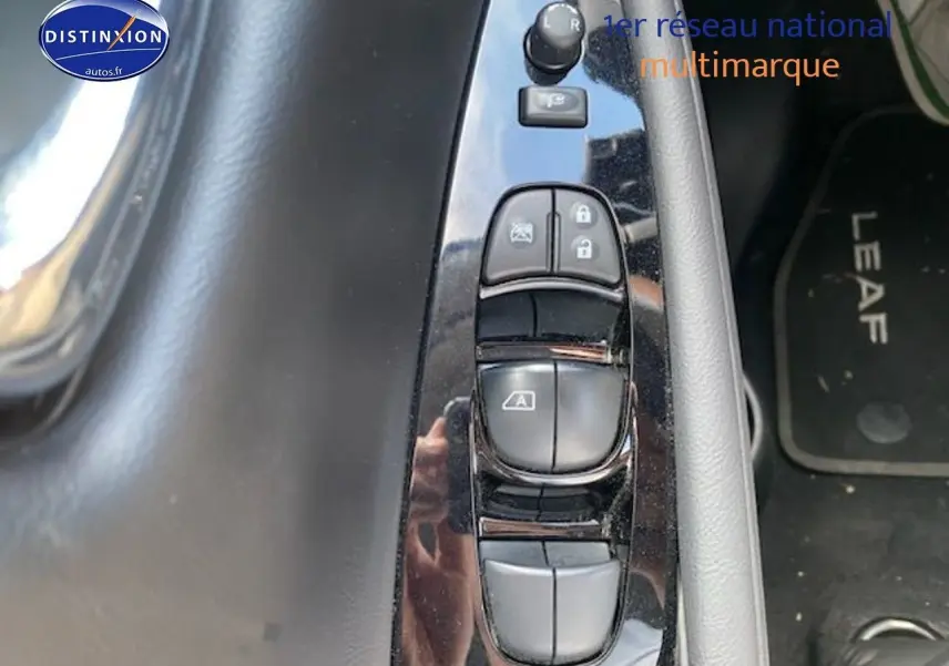 Gros plan sur les commandes de lève-vitres côté conducteur d'une Nissan Leaf blanche nacrée 2019, tapis avec logo Leaf visible.