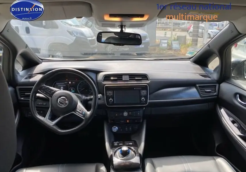 Vue intérieure du tableau de bord et volant du Nissan Leaf blanc nacré, avec écran tactile central et commandes modernes.