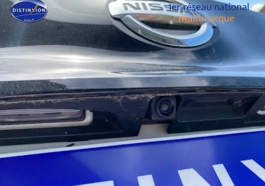 Gros plan sur la caméra de recul intégrée sous le logo Nissan d'une Leaf électrique blanc nacré.