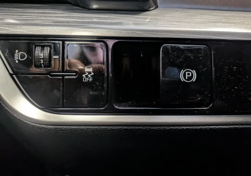 Gros plan sur les commandes noires du tableau de bord du Kia Sportage MY25, boutons ABS et frein de parking électrique.