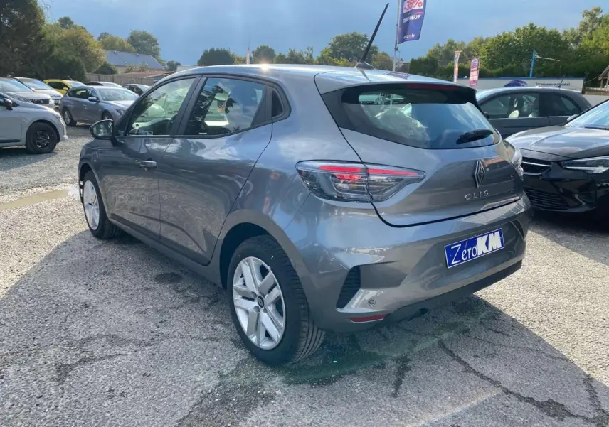 Renault Clio 2025 gris schiste vue 3/4 arrière droit sur parking avec feux LED et plaque Zero KM.