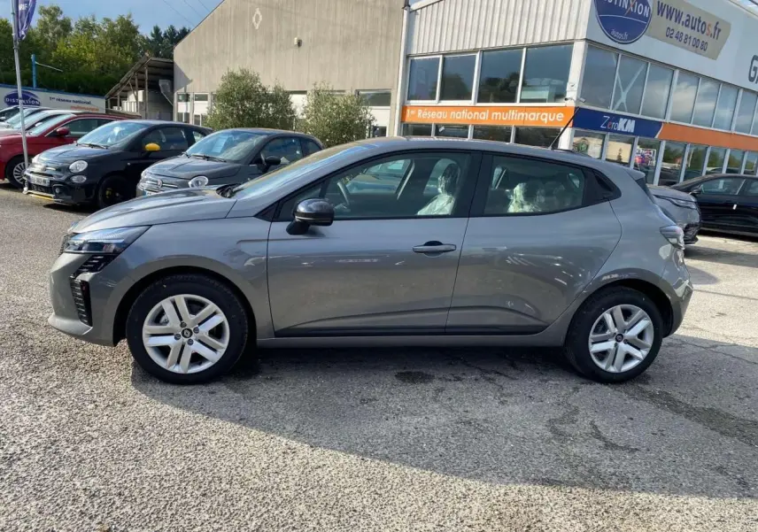 Profil côté gauche d'une Renault Clio 2025 gris schiste garée devant un bâtiment commercial.