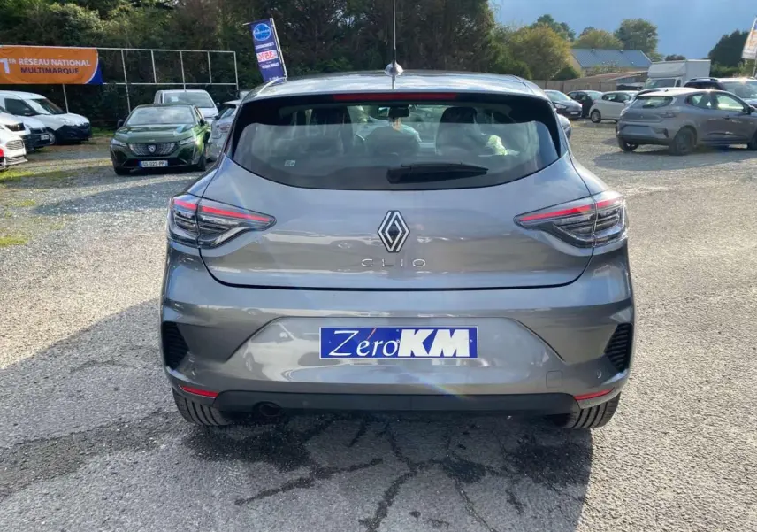 Vue arrière d'une Renault Clio 2025 gris schiste avec feux LED et plaque Zéro KM sur un parking extérieur.