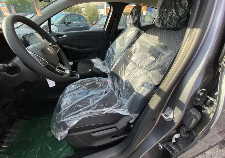 Intérieur côté conducteur d'une Renault Clio 2025 gris schiste, sièges avant protégés par film plastique.