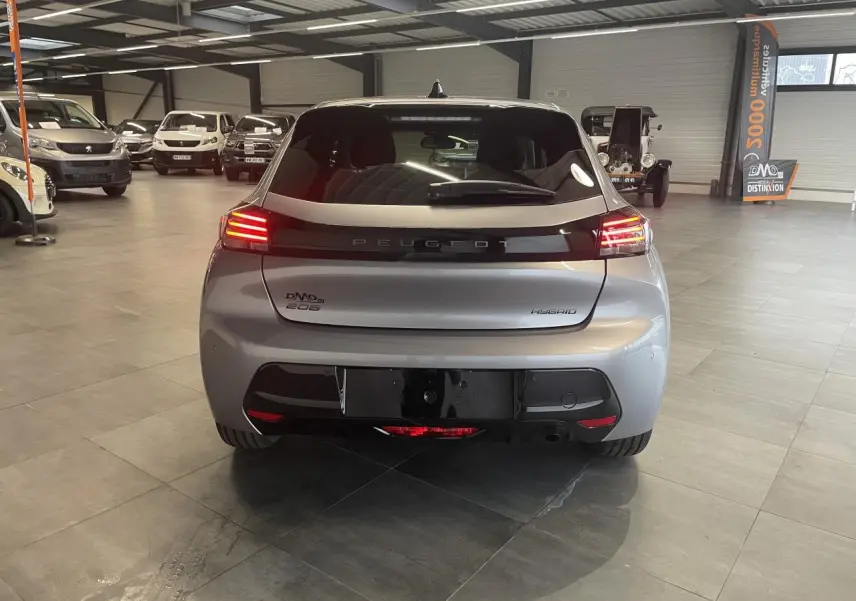 Vue arrière d'une Peugeot 208 hybride gris Artense avec feux arrière à LED allumés en intérieur showroom.