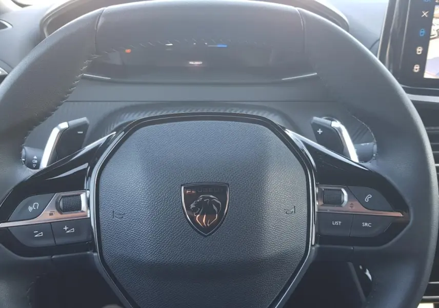 Gros plan sur le volant noir du Peugeot 2008 Hybrid 145 Allure avec commandes intégrées et logo lion central.