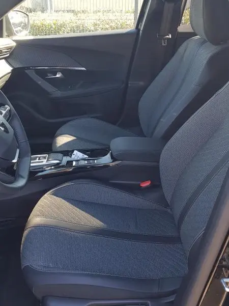 Vue intérieure côté conducteur du Peugeot 2008 Hybrid 145 Allure 2025 noir, sièges tissu gris et console centrale moderne.