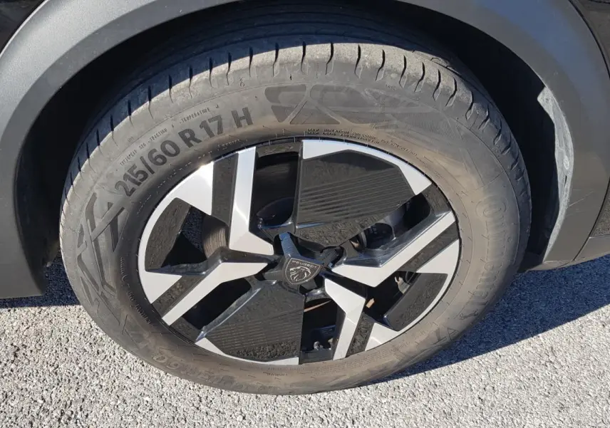 Gros plan sur la jante alliage 17 pouces noire et argentée du côté gauche d’un Peugeot 2008 Hybrid 145 Allure noir.