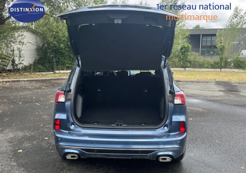Vue arrière d'un Ford Kuga bleu chrome métal 2024 avec coffre ouvert et double sortie d'échappement visible.