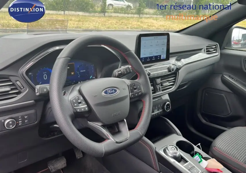 Vue intérieure du tableau de bord et volant du Ford Kuga 2024, finition ST-LINE avec surpiqûres rouges et écran tactile central.