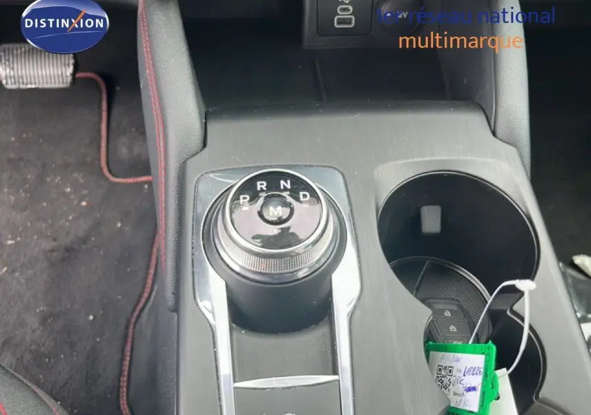 Gros plan sur la molette de boîte automatique et porte-gobelets du Ford Kuga bleu chrome métal, intérieur noir avec surpiqûres rouges.