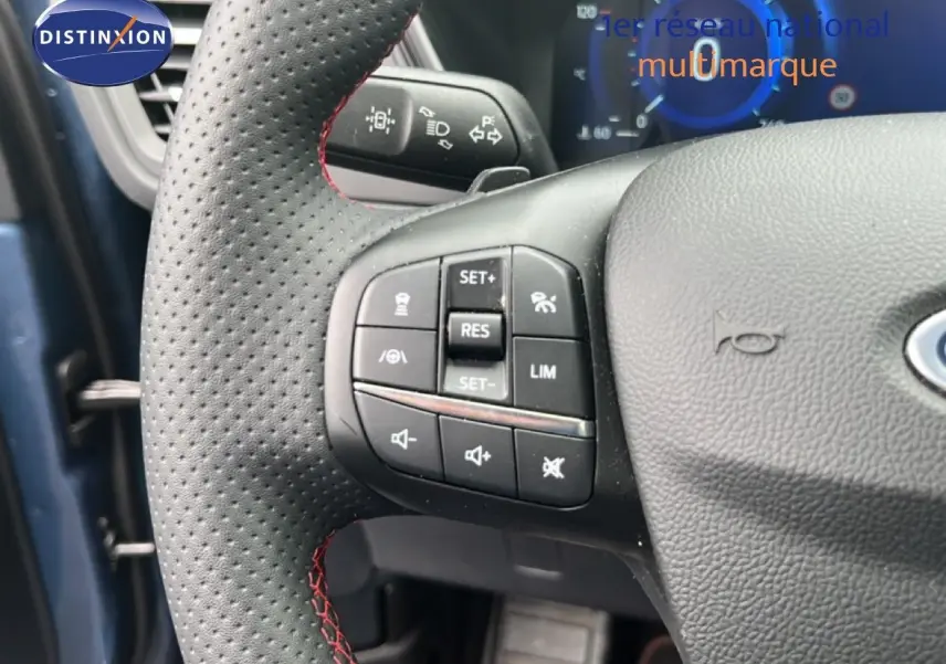 Gros plan sur le volant perforé avec surpiqûres rouges du Ford Kuga 2024 bleu chrome, montrant les commandes multifonctions à gauche.