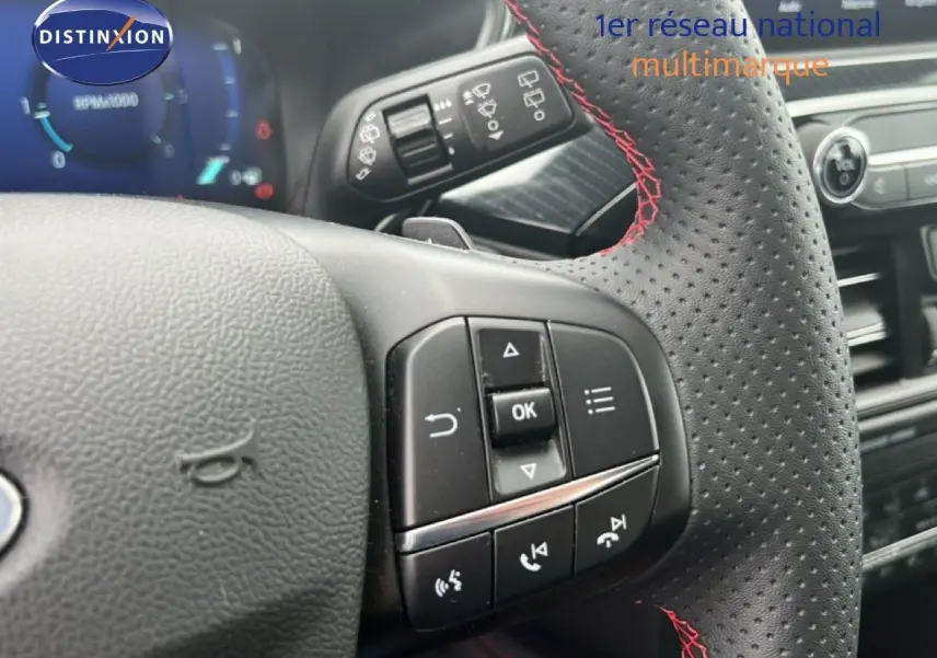 Gros plan sur le volant perforé avec surpiqûres rouges du Ford Kuga 2024 bleu chrome, montrant les commandes multifonctions.