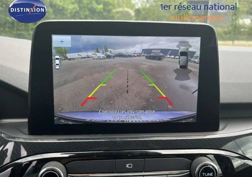 Écran central montrant la caméra de recul du Ford Kuga bleu chrome, avec les lignes de guidage colorées visibles.