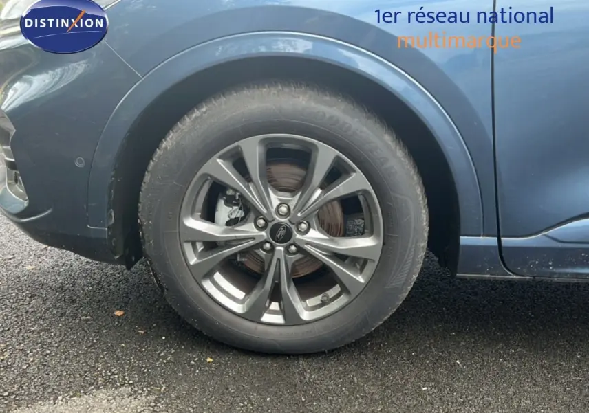 Gros plan sur la roue avant droite d’un Ford Kuga bleu chrome métal, mettant en valeur la jante alliage et le passage de roue.