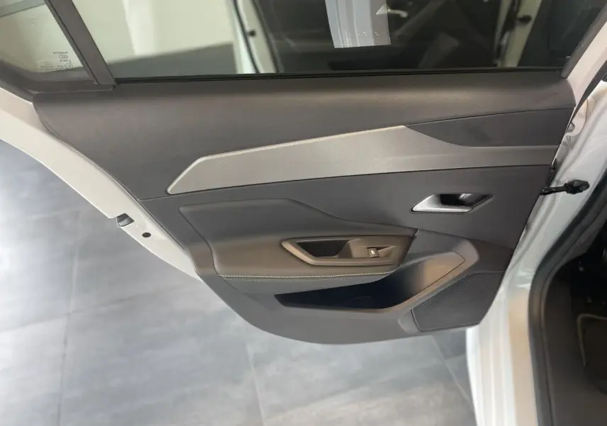 Porte arrière gauche ouverte d'une Peugeot 308 blanche, avec garniture noire et insert gris clair texturé.