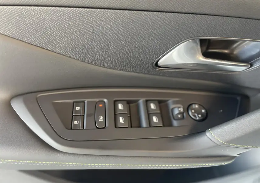 Gros plan sur la commande des vitres et rétroviseurs côté conducteur de la Peugeot 308 blanche, avec surpiqûres vertes.
