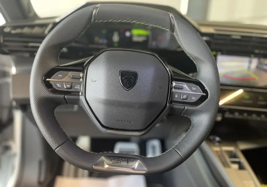 Volant cuir noir Peugeot 308 GT 2025 vu de face avec commandes intégrées et logo lion central.
