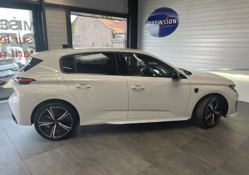 Peugeot 308 blanche vue de profil côté gauche en intérieur avec jantes alliage noires et vitres teintées.