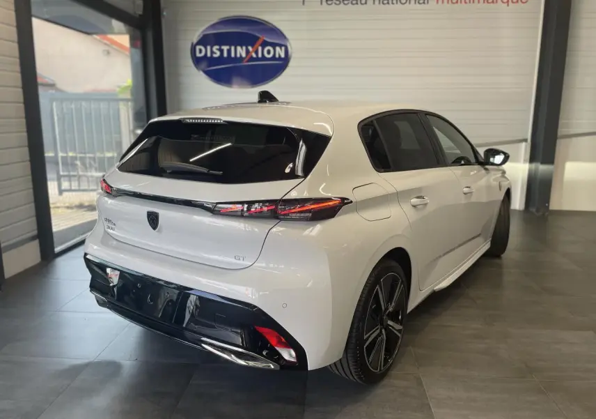 Vue 3/4 arrière droite d'une Peugeot 308 GT blanche avec feux arrière LED et jantes alliage 18 pouces en showroom.