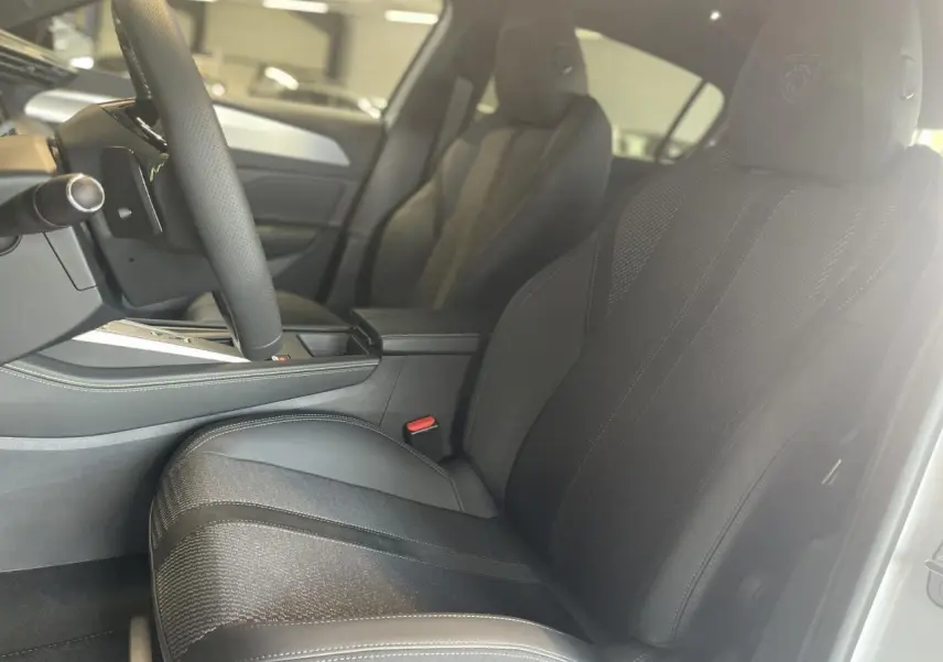 Intérieur de la Peugeot 308 GT 2025, vue côté conducteur sur sièges tissu/TEP noirs avec logo Peugeot brodé.