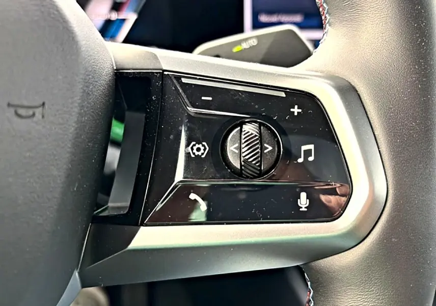 Gros plan sur les commandes multifonctions noires et argentées du volant cuir de la BMW Série 5 i5 M60 2024.