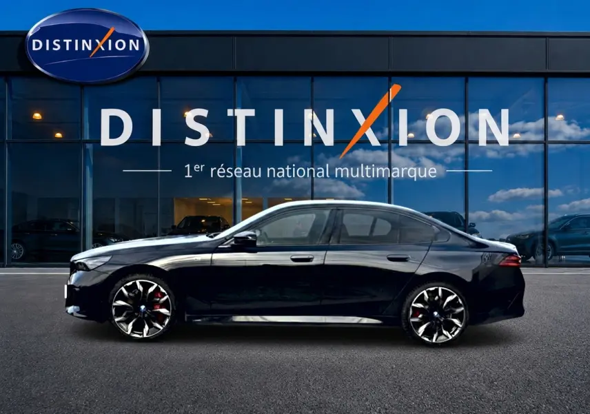 Profil latéral gauche d'une BMW Série 5 i5 M60 noire avec jantes alu bicolores devant un showroom Distinxion.