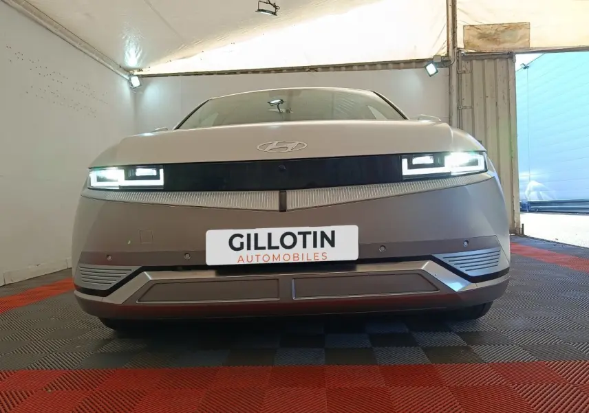 Vue frontale d'une Hyundai IONIQ BEV 77KWH AWD Executive beige avec phares LED allumés dans un garage.