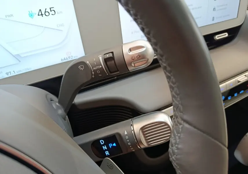 Gros plan sur le levier de vitesses et commandes au volant en cuir gris d’une Hyundai IONIQ BEV beige, tableau de bord numérique visible.