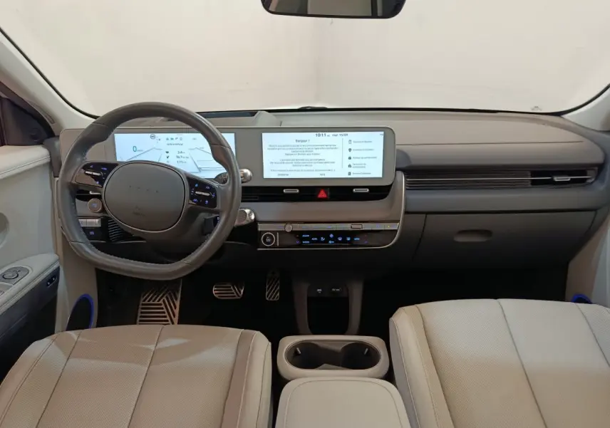 Vue intérieure avant de la Hyundai IONIQ BEV beige 2023, tableau de bord moderne avec double écran tactile et volant cuir.