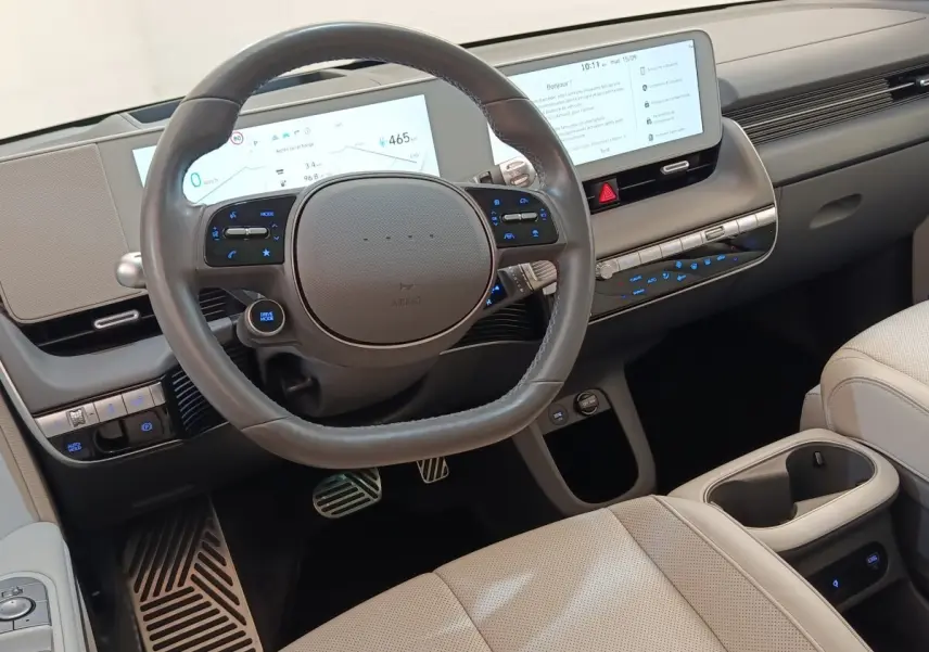 Vue intérieure centrée sur le volant cuir et tableau de bord numérique de la Hyundai IONIQ BEV beige 2023.