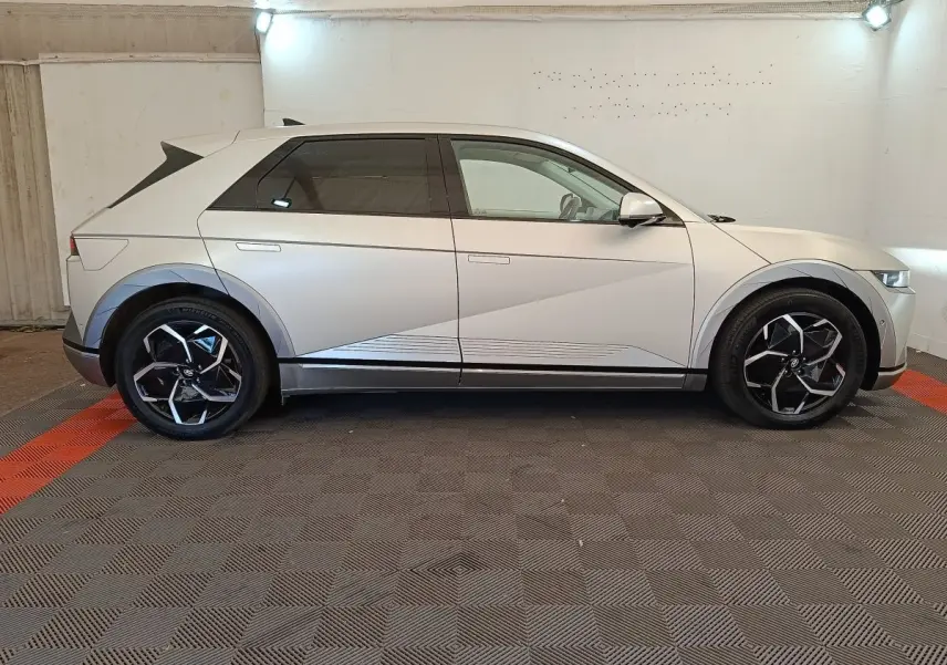 Vue de profil côté gauche d'une Hyundai IONIQ électrique beige 2023 avec jantes noires et détails géométriques sur la carrosserie.