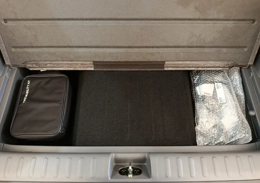 Coffre ouvert de Hyundai IONIQ beige 2023, vue plongeante sur espace de rangement avec kit de mobilité et accessoires emballés.