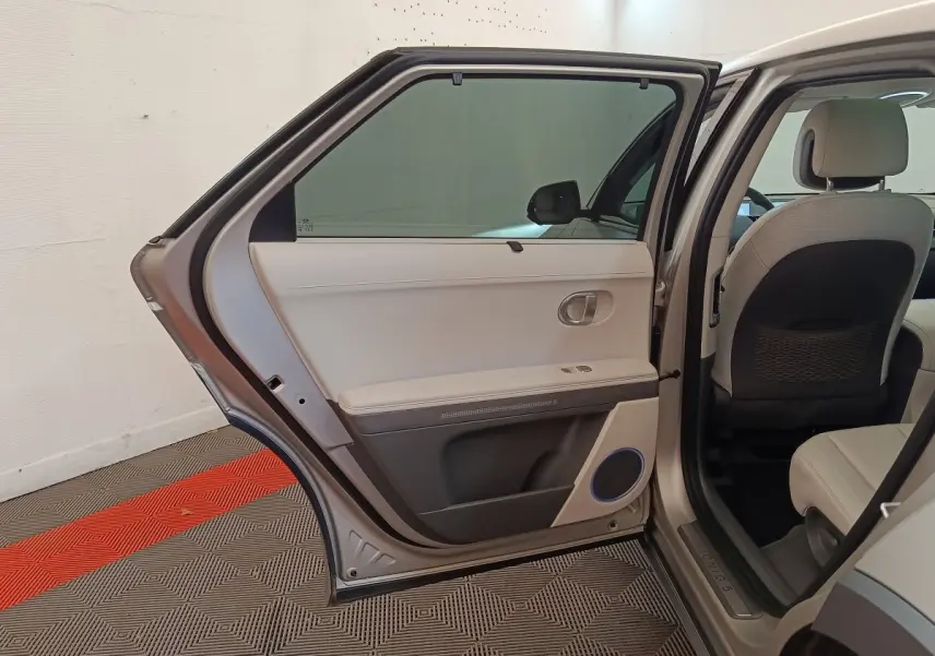 Vue intérieure côté gauche arrière d'une Hyundai IONIQ beige 2023, porte ouverte montrant la garniture claire et les sièges assortis.