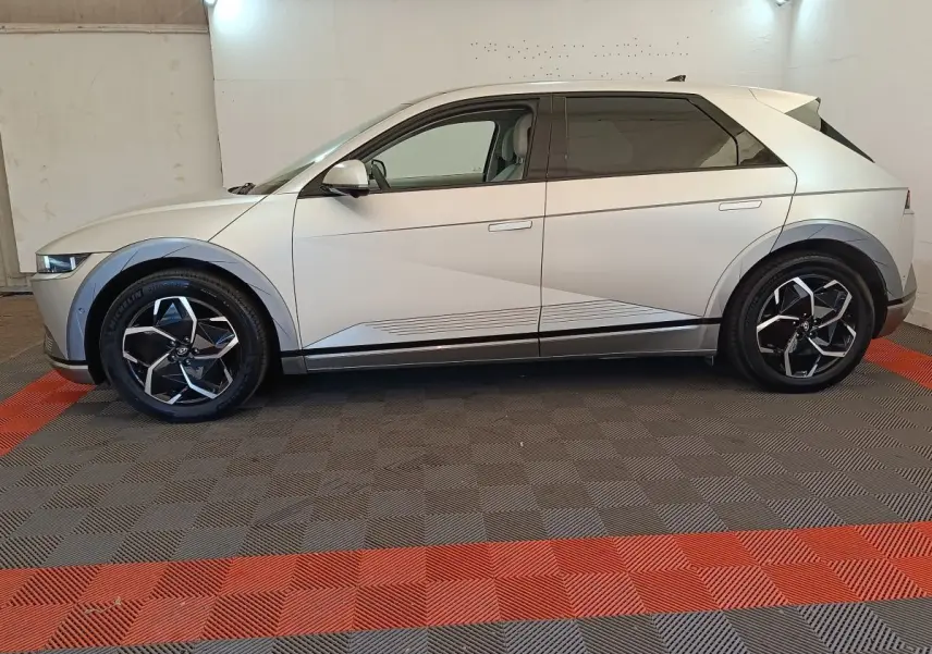 Vue de profil côté gauche d'une Hyundai IONIQ électrique beige 2023 avec jantes noires et détails géométriques sur la carrosserie.