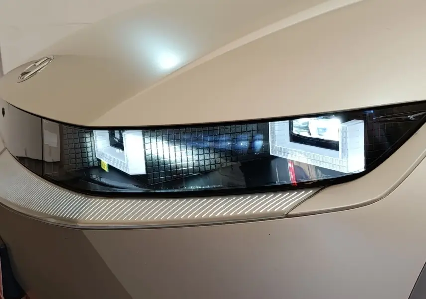 Gros plan sur le phare avant droit allumé d'une Hyundai IONIQ beige électrique, soulignant son design moderne.