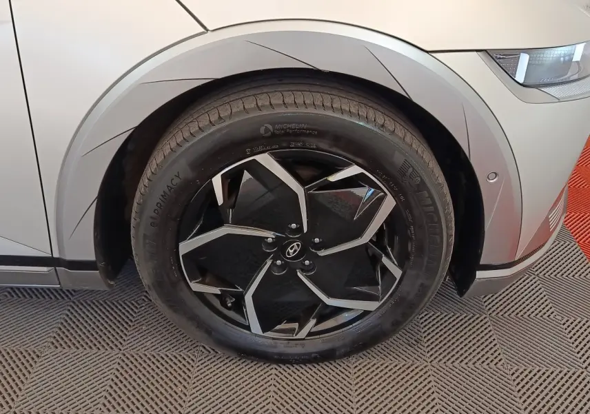 Gros plan sur la roue avant gauche noire et argentée d'une Hyundai IONIQ beige, avec partie avant droite visible.