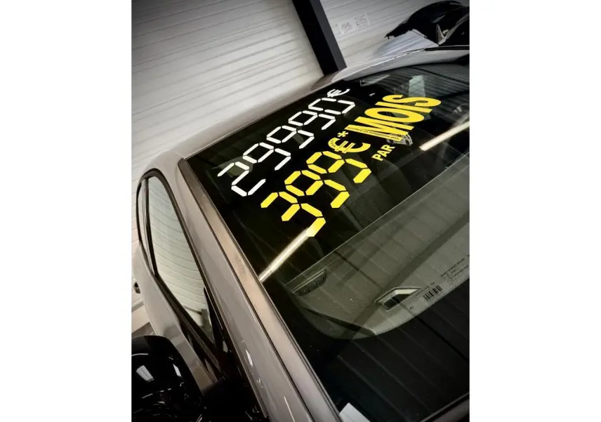 Vue en plongée du côté gauche d'une Peugeot 308 gris selenium avec marquage promotionnel sur le pare-brise